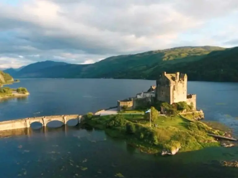 Eilean Donan Castle in the Scottish Highlands surrounded by scenic mountains and water, featured in Braw Scottish Tours video promoting castle tours in Scotland