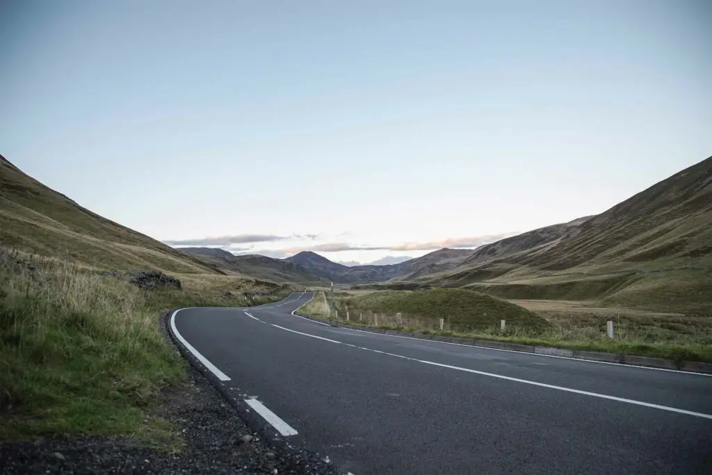 Scenic driving road through the Cairngorms mountains in Scotland with rolling hills and open countryside under a clear sky