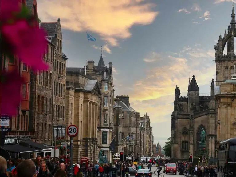 Busy evening view of the historic Edinburgh Royal Mile with tourists, heritage buildings, and St Giles’ Cathedral under a colorful sky in Edinburgh, Scotland