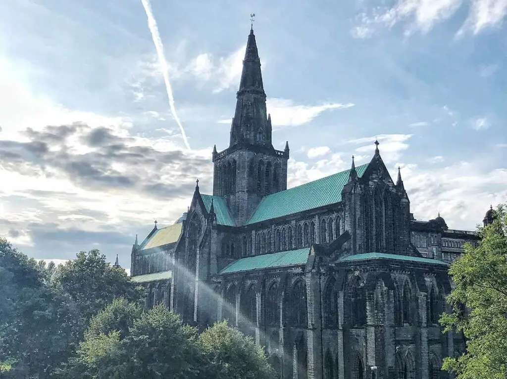 Glasgow Cathedral in Scotland with sunlight streaming through clouds, showcasing historic Gothic architecture and popular tourist attraction in Glasgow