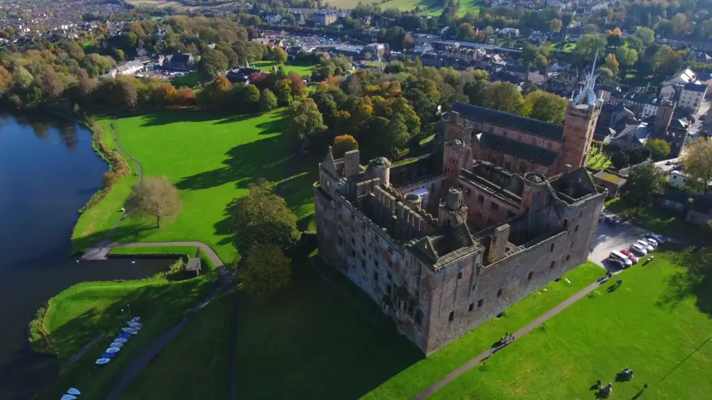Aerial view of Linlithgow Palace in Scotland surrounded by green parkland and Linlithgow Loch, a popular historic tourist attraction near Edinburgh