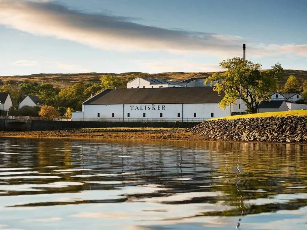 Talisker Whisky Distillery in Carbost, Scotland, viewed from the waterfront with scenic hills and reflections on the water