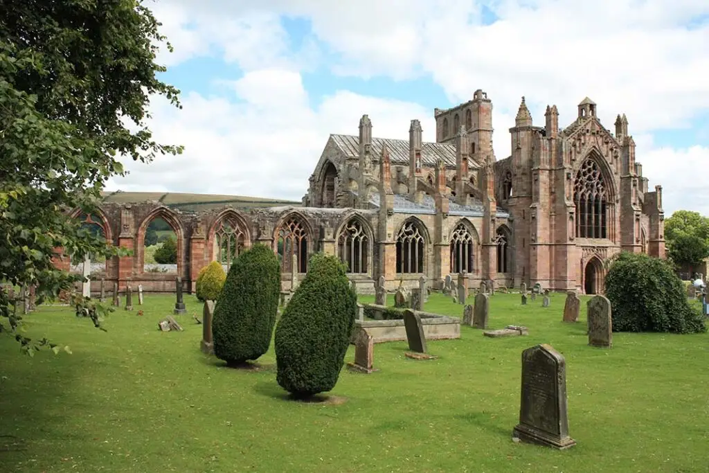 Historic Melrose Abbey ruins in the Scottish Borders, Scotland, showcasing Gothic architecture and ancient gravestones surrounded by green countryside