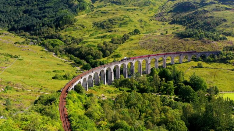 Steam train crossing the Glenfinnan Viaduct surrounded by green hills in the Scottish Highlands, Scotland tours attraction