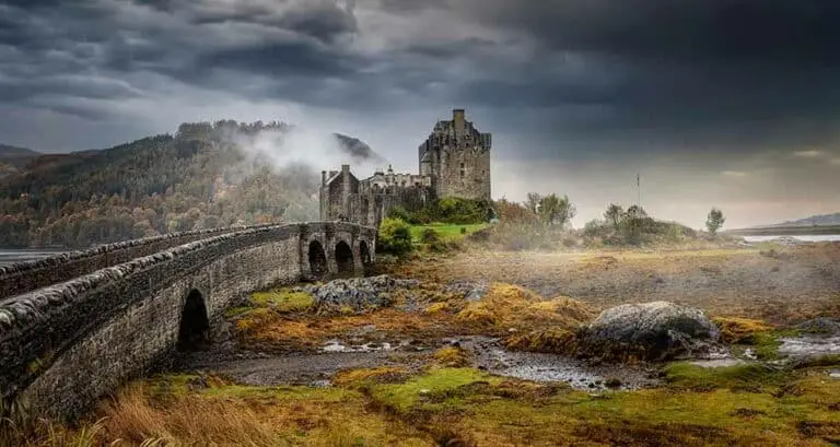 Eilean Donan Castle in the Scottish Highlands with stone bridge and misty dramatic sky, popular Scotland tourist attraction and historic landmark