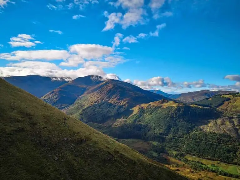 Scenic mountain landscape of Nevis Range in Scotland with lush green hills, forests, and blue sky, popular destination for hiking and outdoor tours