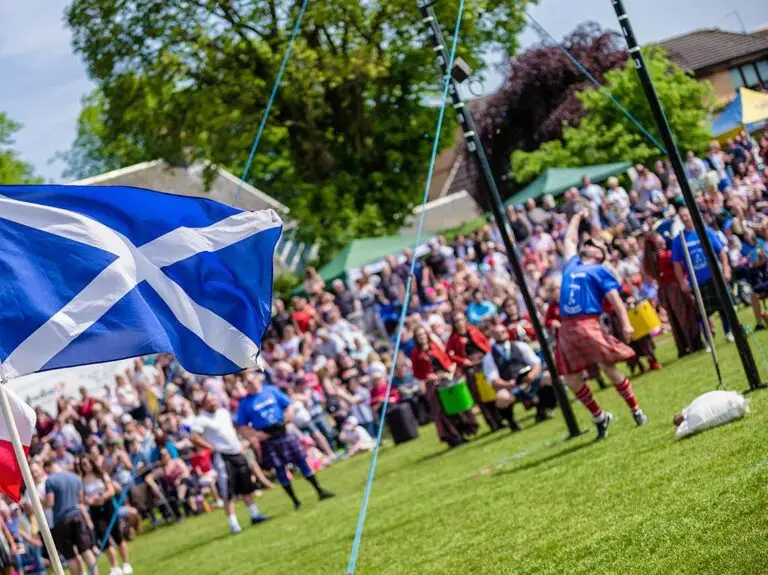 Athletes competing in traditional Highland Games event in Scotland with the Scottish flag and spectators in the background