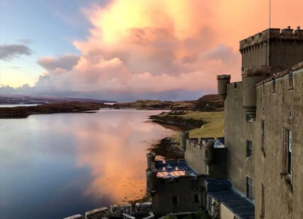 Dunvegan Castle on the Isle of Skye, Scotland, overlooking a calm loch at sunset with vibrant clouds in the sky