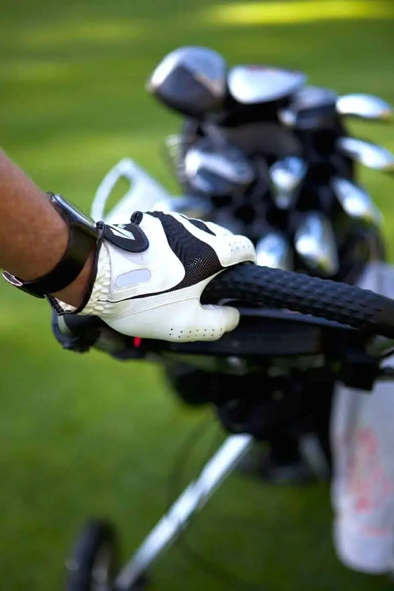 Golfer wearing a glove holding a golf trolley handle with golf clubs in the background at St Andrews, Scotland