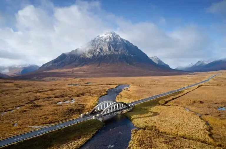 Scenic view of Glencoe Valley in the Scottish Highlands with Buachaille Etive Mòr mountain, a winding river, and a bridge under clear blue skies, Scotland