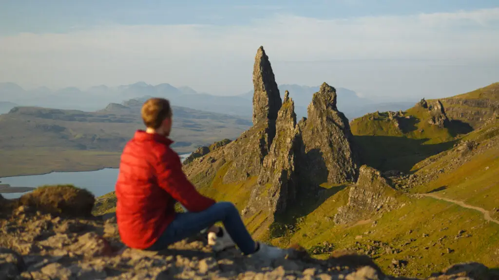 Traveler admiring the Old Man of Storr rock formation on the Isle of Skye in Scotland with scenic mountain and coastal landscape in the background