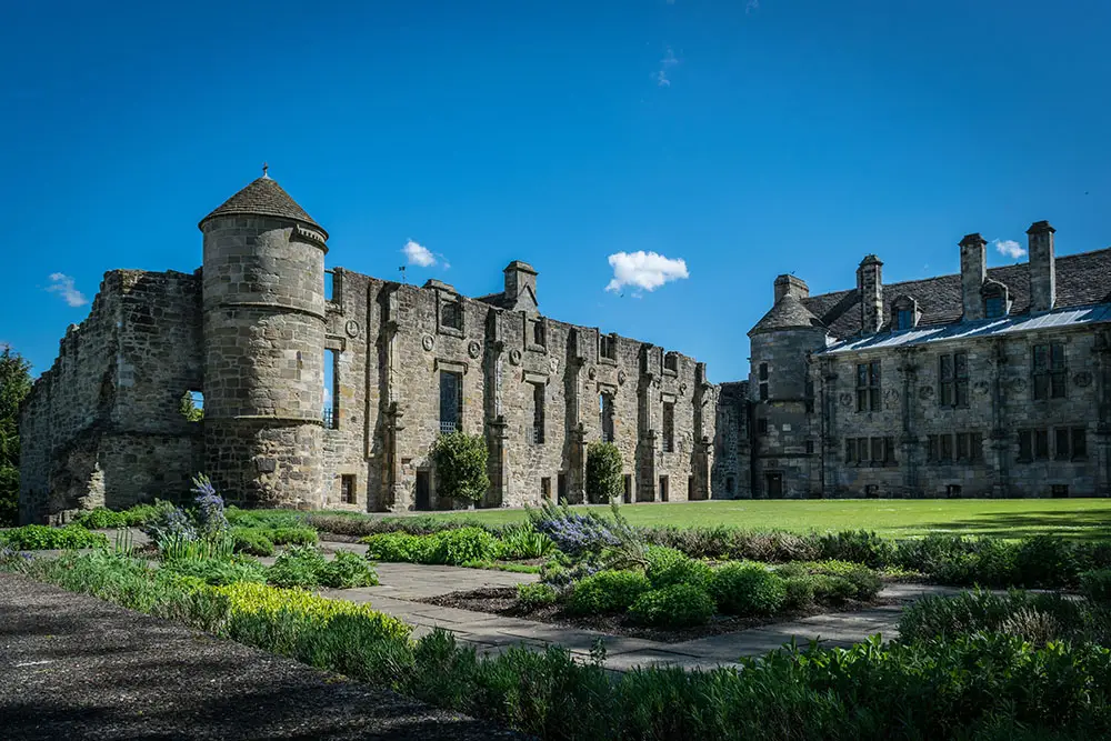 Historic Falkland Palace in Fife, Scotland, with stone architecture, lush gardens, and blue sky, a popular tourist attraction on Braw Scottish Tours.