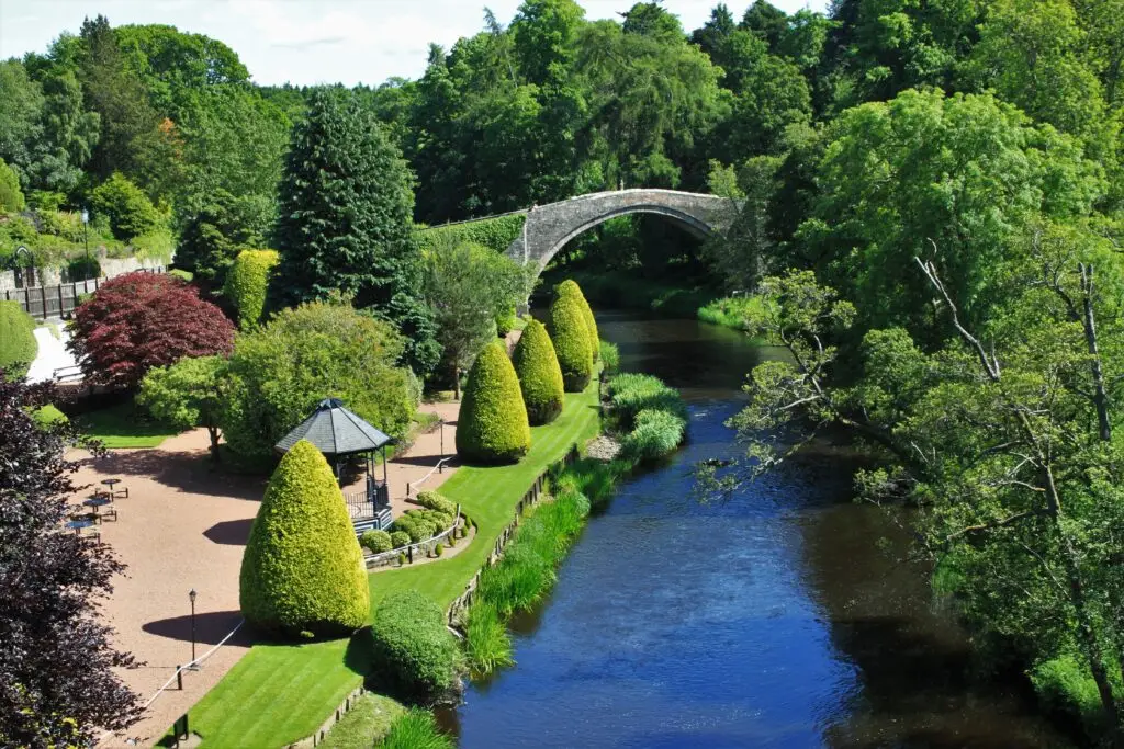 Picturesque view of the Brig o’ Doon stone bridge over the River Doon surrounded by lush greenery and gardens in Alloway, Scotland