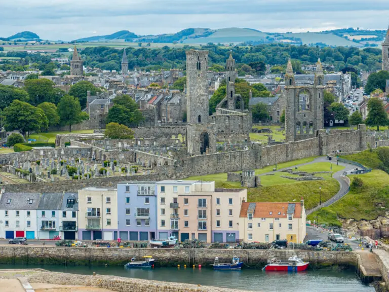 St Andrews Cathedral ruins overlooking colorful waterfront buildings and harbor in St Andrews, Scotland, a popular historic tourist destination on the Fife coast