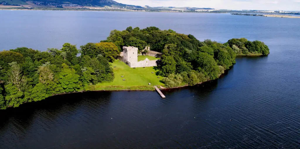 Aerial view of Loch Leven Castle on a small island surrounded by water and greenery in Kinross, Scotland, a historic Scottish tourist attraction.