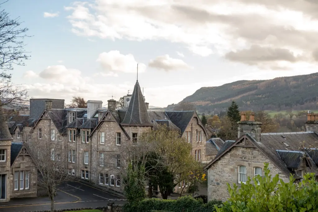 Historic stone buildings in Pitlochry, Scotland with scenic hillside landscape in the background, showcasing traditional Scottish architecture and countryside charm