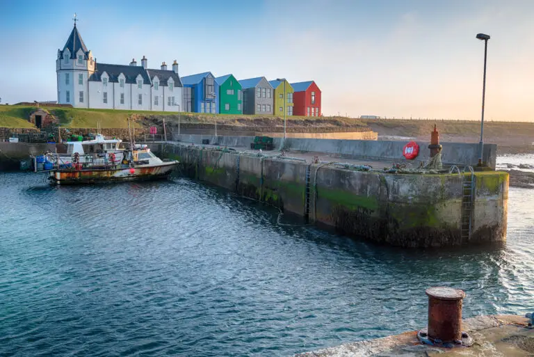 Fishing boat at the harbor in John o’ Groats, Scotland, with colorful waterfront houses and coastal scenery at sunset