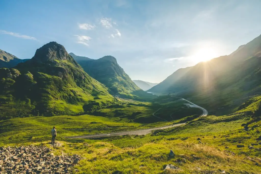 Scenic view of Glencoe valley in the Scottish Highlands with a person admiring the mountains and winding road at sunrise, popular destination for tours in Scotland