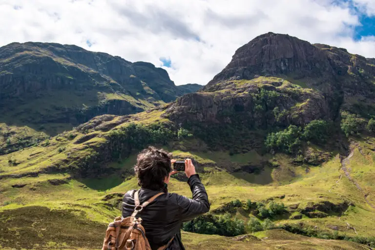 Tourist taking a photo of the scenic mountains and green landscape in Glencoe, Scotland