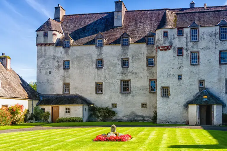 Historic Traquair House in Scotland with manicured gardens and stone architecture under a blue sky, popular tourist attraction on Braw Scottish Tours