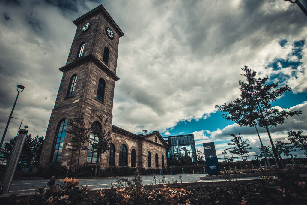Historic clock tower building with modern glass extension under dramatic sky in Glasgow, Scotland