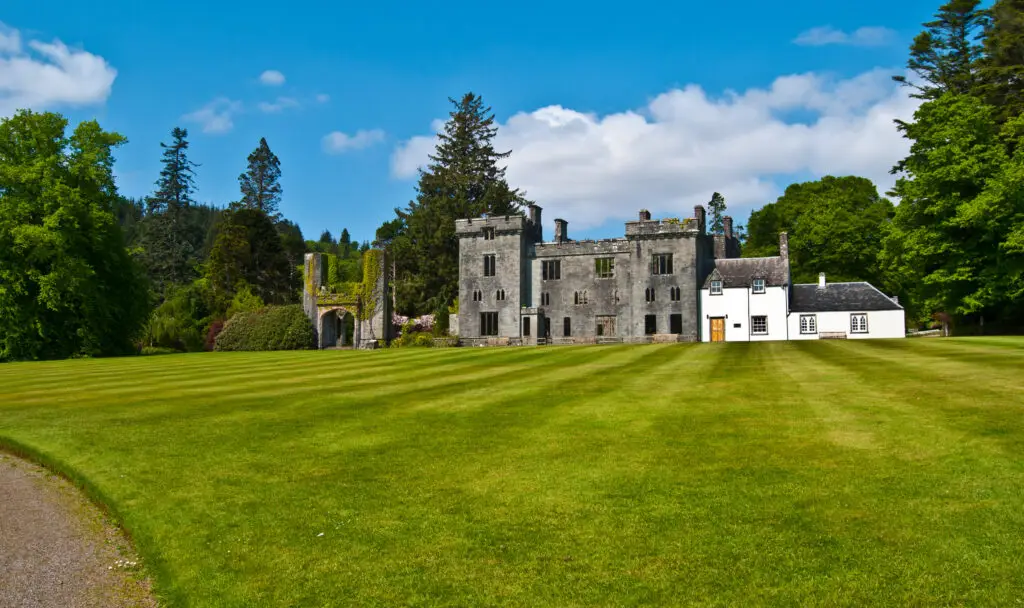 Armadale Castle Gardens on the Isle of Skye in Scotland featuring historic castle ruins, landscaped lawns, and lush green trees under a bright blue sky