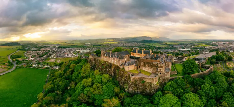 Aerial view of Stirling Castle in Scotland surrounded by lush greenery and overlooking the city of Stirling, a popular historic tourist attraction in the Scottish Highlands.