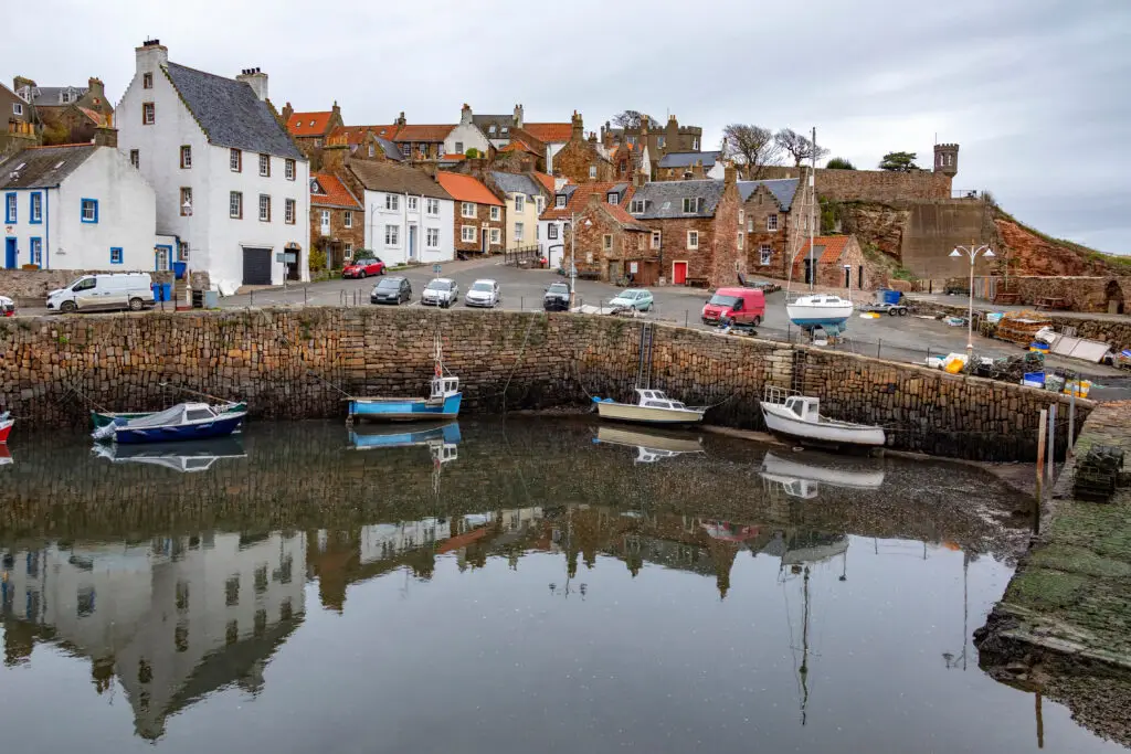 Colourful fishing boats moored in the historic harbour of Crail, a picturesque coastal village in Fife, Scotland, with traditional stone houses and waterfront scenery.