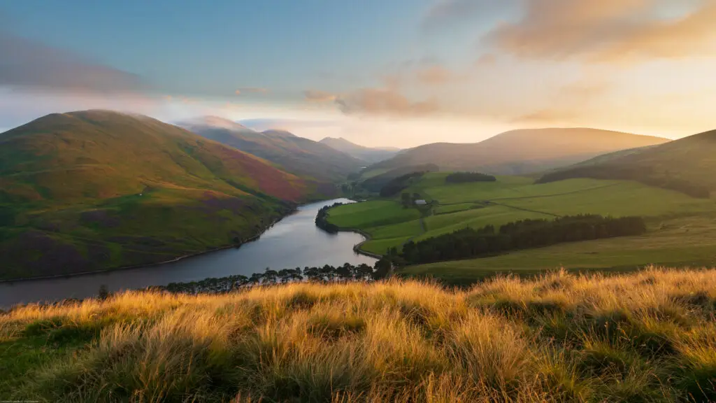 Scenic view of Pentland Hills in Scotland with rolling green hills, a winding river, and golden sunset light illuminating the landscape, popular destination for hiking and nature tours near Edinburgh