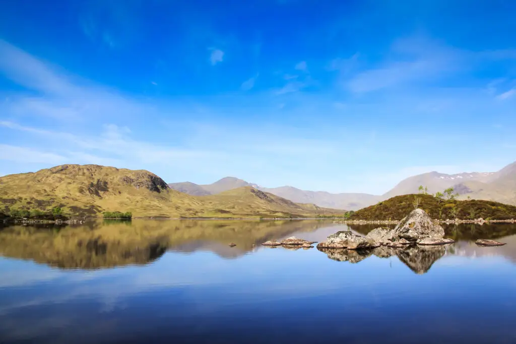Scenic view of Rannoch Moor in the Scottish Highlands with calm reflective water, rugged hills, and clear blue sky, showcasing natural beauty and landscape of Scotland