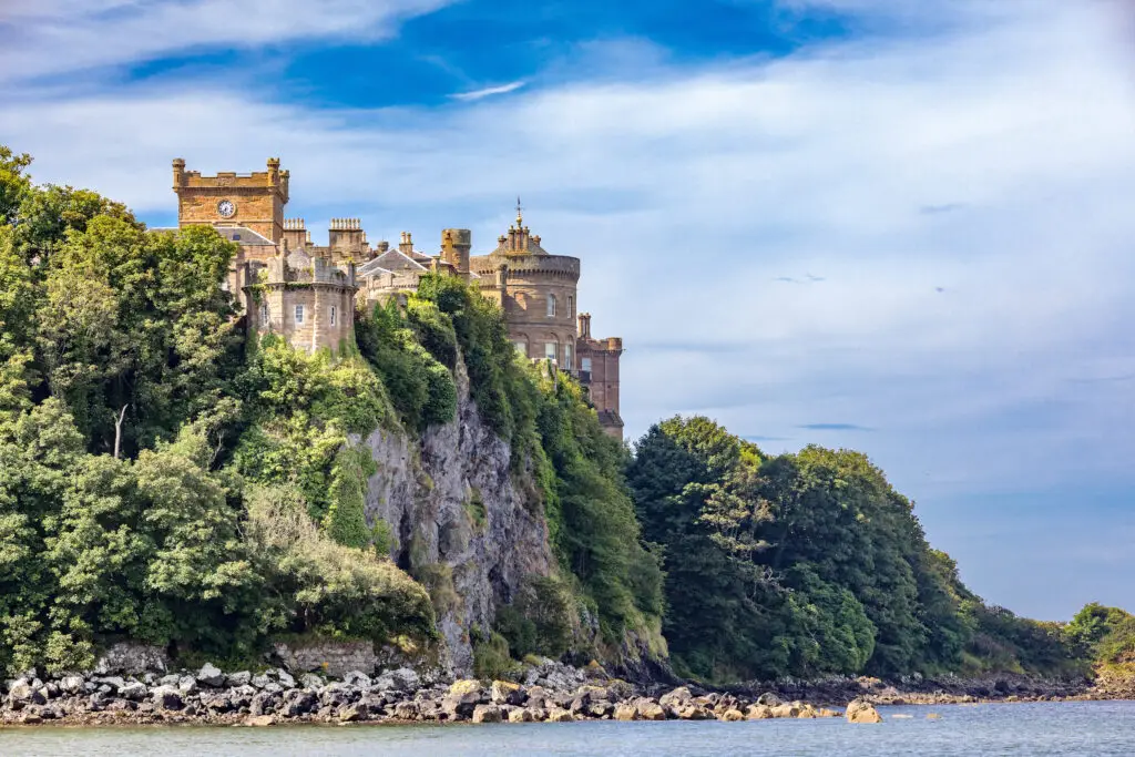 Culzean Castle perched on a cliff overlooking the sea in Ayrshire, Scotland, surrounded by lush greenery and blue sky, a popular Scottish tourist attraction and historic site