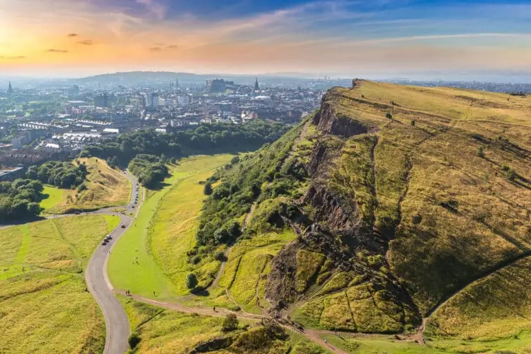Panoramic view of Edinburgh, Scotland from Arthur’s Seat showing the city skyline, historic landmarks, and lush green hills at sunset