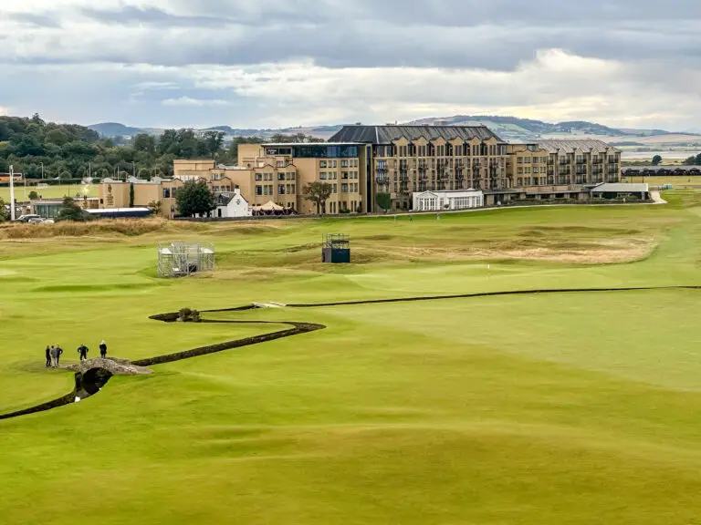 View of the Old Course golf course and the Swilcan Bridge at St Andrews, Scotland, with the Old Course Hotel in the background under a cloudy sky