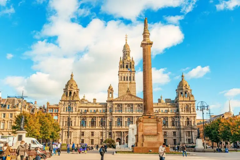 George Square and Glasgow City Chambers in Glasgow, Scotland, with people walking and relaxing on a sunny day