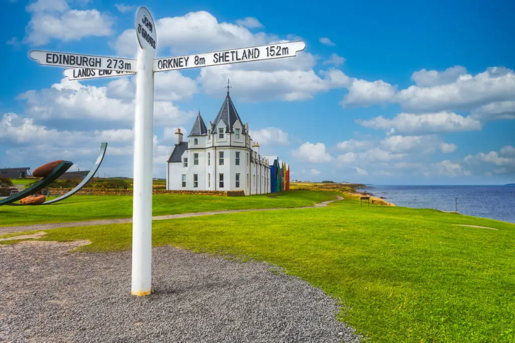 Iconic John O’Groats signpost with coastal scenery and traditional Scottish building overlooking the sea in Caithness, Scotland