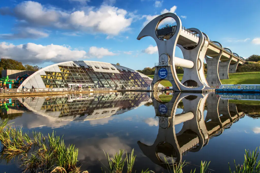 The Falkirk Wheel boat lift reflecting in the canal water on a sunny day in Falkirk, Scotland, a popular engineering landmark and tourist attraction