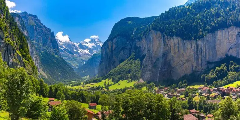 Panoramic view of Lauterbrunnen Valley in Switzerland with alpine mountains, green meadows, waterfalls, and a picturesque village under clear blue skies